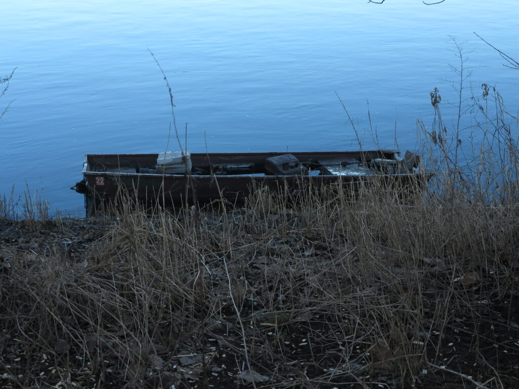 an empty boat on the edge of the water, slightly concealed by grass