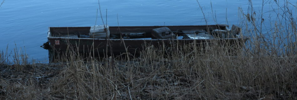 an empty boat on the edge of the water, slightly concealed by grass